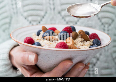 Nahaufnahme von Frau Essen Schüssel Haferbrei mit Früchten und Nüssen für gesundes Frühstück Stockfoto