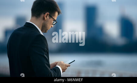 Junge Unternehmer verwendet Smartphone beim Stehen auf der Straße mit großen Wolkenkratzer. Stockfoto