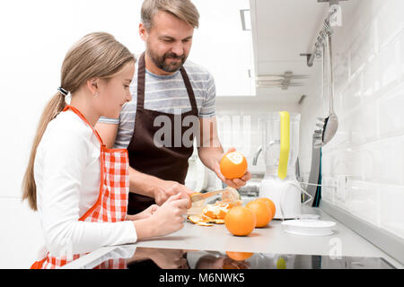 Seitenansicht Porträt Der glückliche Vater kochen mit Tochter, Orangensaft in der modernen Küche zu Hause. Stockfoto