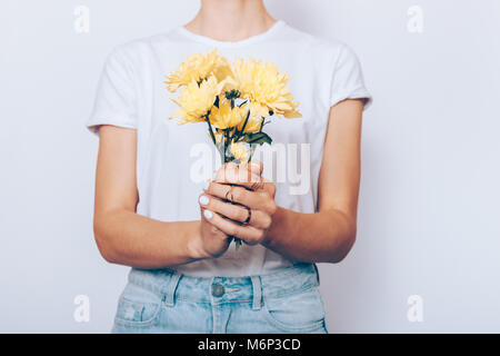 Frau, die in einem T-Shirt und Jeans hält einen Strauß gelber Blumen auf weißem Hintergrund Stockfoto