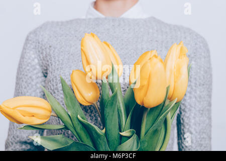 Zugeschnittenes Bild eines Strauß gelber Tulpen und eine Frau in einem grauen pullover, close-up Stockfoto