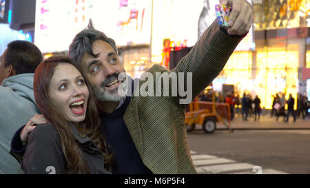 Paar nehmen selfie Foto mit Smart Mobile Handy am Times Square in New York City bei Nacht unter dem hellen Neonlichter aufgeregt. Reisen Touristen Stockfoto