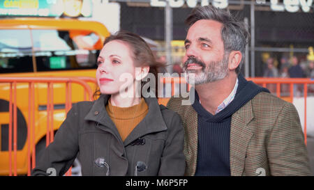 Zwei junge Freunde sitzen auf New York City street Bank anzeigen großes Neon Plakate und helle Lichter am Times Square. Gelbe taxi Antriebe durch. Stockfoto