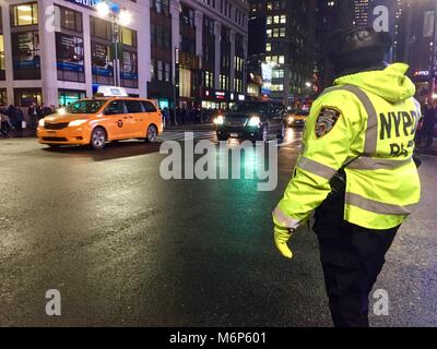 New York City - ca. 2017: NYPD Traffic Polizist steht Patrol Regie Berufsverkehr in geschäftigen Midtown Manhattan bei Nacht. Gelbe Taxi Stockfoto