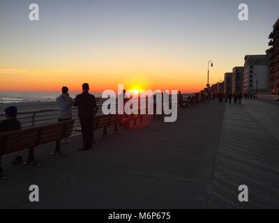Schönen Sonnenuntergang über dem Meer auf einem Coastal Promenade der Stadt. Leute trainieren, auf Boardwalk stoppen die Sonne über dem Wasser Horizont zu sehen Stockfoto