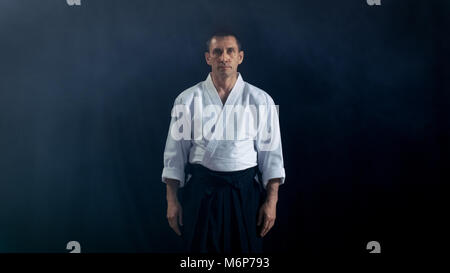 Portraitfotos der Aikido Master tragen traditionelle Samurai Hakama Kleidung in die Kamera schaut. Er ist in den Mittelpunkt der Finsternis Ihn umgibt. Stockfoto