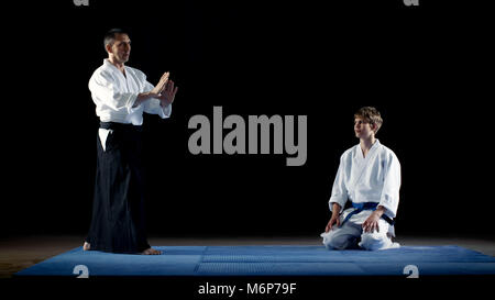 Martial Arts Master zeigt wunderschöne Aikido Kampftechniken an seinen Schüler die ihn mit Respekt sieht. Schuß isoliert auf die Schwarze Stockfoto