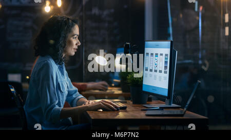Schöne weibliche Coder arbeitet an Ihrem Desktop auf Ihrem Peropnal Computer. Ihr männlicher Kollege sitzt neben ihr. Abends Office hat Creative Lighting. Stockfoto
