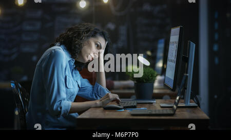 Müde, überarbeitete weiblichen Finanzier hält Ihren Kopf in die Hände während der Arbeit auf einem PC. Im Hintergrund kreative Büro. Stockfoto