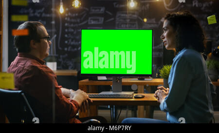 Schöne weibliche Mitarbeiter an Ihrem Schreibtisch Gespräche mit ihren männlichen Kollegen auf dem Schreibtisch steht Computer mit Mock-up Green Screen. Stockfoto