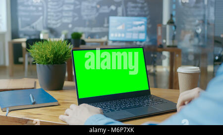 Männliche Mitarbeiter an seinem Schreibtisch arbeitet auf einem Laptop mit Mock-up Green Screen. Über der Schulter Close-up Aufnahmen. Im Hintergrund kreative Büro. Stockfoto