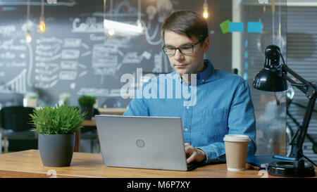 Hübscher junger Büro Mitarbeiter arbeitet auf einem Laptop. Er arbeitet in der Kreativen stilvolle Büro. Stockfoto