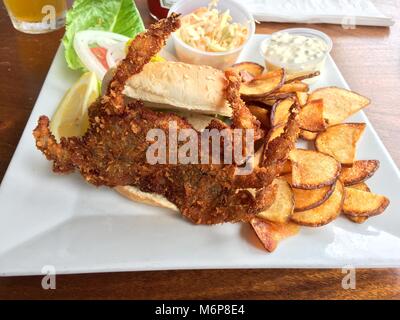 Lecker gebratene Soft Shell Crab Sandwich auf Sesam Brötchen mit frischen Kartoffelchips, cole slaw, Remoulade und Zitrone auf einem Gourmet weiße Platte serviert. Stockfoto