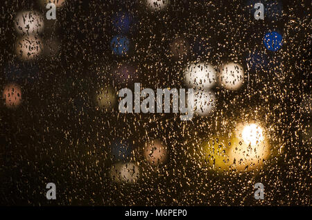 Regentropfen auf dem Fenster auf dem Hintergrund der Nacht. Emotionale romantisch Abstrakt Hintergrund mit Defokussierten leuchtet. Konzentrieren Sie sich auf wenige Tropfen Stockfoto