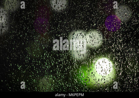Regentropfen auf dem Fenster auf dem Hintergrund der Nacht. Emotionale romantisch Abstrakt Hintergrund mit Defokussierten leuchtet. Konzentrieren Sie sich auf wenige Tropfen Stockfoto