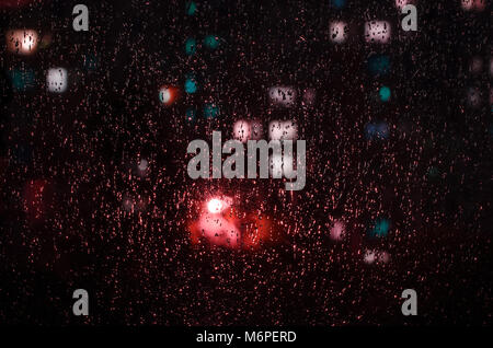 Regentropfen auf dem Fenster auf dem Hintergrund der Nacht. Emotionale romantisch Abstrakt Hintergrund mit Defokussierten leuchtet. Konzentrieren Sie sich auf wenige Tropfen Stockfoto