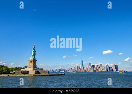 Die Freiheitsstatue im Vordergrund mit unverwechselbaren New York Manhattan Skyline im Hintergrund über den Hudson und gegen einen strahlend blauen Himmel gesehen Stockfoto