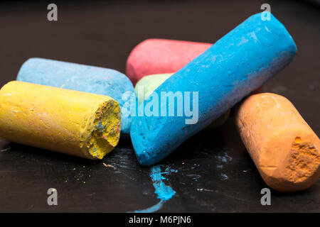 Stapel der Farbstifte in verschiedenen Farben auf einem schwarzen Hintergrund Tafel Stockfoto