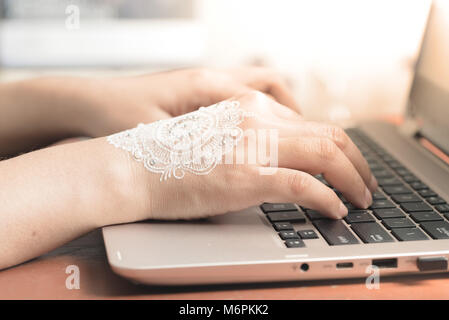 Frau Hand mit Henna Tippen auf Laptop Tastatur. Business Konzept oder eine Frau arbeiten von zu Hause Büro nach Hochzeit Feier Stockfoto