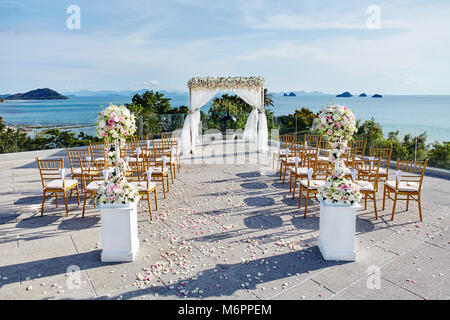 Hochzeit, arch mit Blumen Dekoration, Chiavari gold Stühle Setup, Rosen Blüten auf dem Gang zu Fuß weg, Ozean Hintergrund Stockfoto