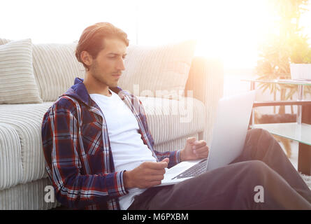 Moderne Kerl mit einem Laptop auf den Boden neben das Sofa Stockfoto
