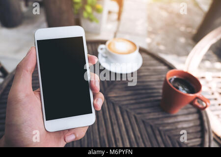 Mockup Bild der Hände des Menschen Holding white Handy mit leeren schwarzen Bildschirm im Coffee Shop Stockfoto