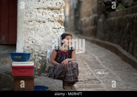 Ein junger einheimischer, ethnischen Tz'utujil Maya Mädchen in traditioneller Kleidung vor ihrem Haus sitzen. Santiago de Atitlán, Departement Sololá, Guatemala. Stockfoto