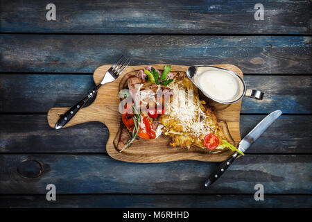 New York Steak mit Kartoffelpuffer im rustikalen Board mit Besteck und Holz- Hintergrund, Ansicht von oben. Stockfoto