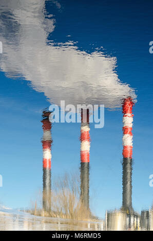 Die rauchenden Schornsteine der Anlage sind im Wasser wider. Die Leitungen mit den Rauch gegen den klaren blauen Himmel. Zusammenfassung Hintergrund mit Verzerrung der Re Stockfoto