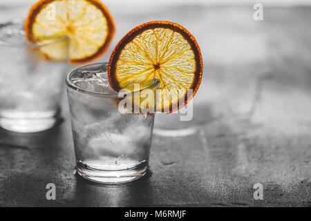 Zwei Schüsse von Tequila mit Eis und eine getrocknete orange Slice auf grauem Hintergrund.