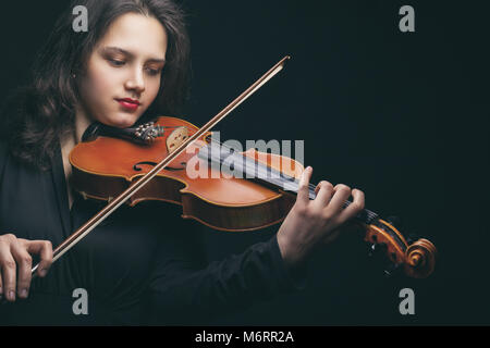Schöne junge Frau spielt die Geige auf dunklem Hintergrund Stockfoto