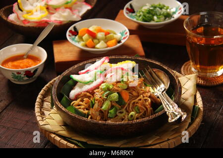 Mie Goreng Jawa. Unter Rühren gebratene Eiernudeln mit Weißkohl, Karotten, Frikadellen, und süße Sojasauce. Mit Crackern, Chili Sauce und Gurken serviert. Stockfoto