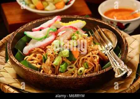 Mie Goreng Jawa. Unter Rühren gebratene Eiernudeln mit Weißkohl, Karotten, Frikadellen, und süße Sojasauce. Mit Crackern, Chili Sauce und Gurken serviert. Stockfoto