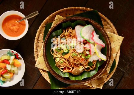 Mie Goreng Jawa. Unter Rühren gebratene Eiernudeln mit Weißkohl, Karotten, Frikadellen, und süße Sojasauce. Mit Crackern, Chili Sauce und Gurken serviert. Stockfoto