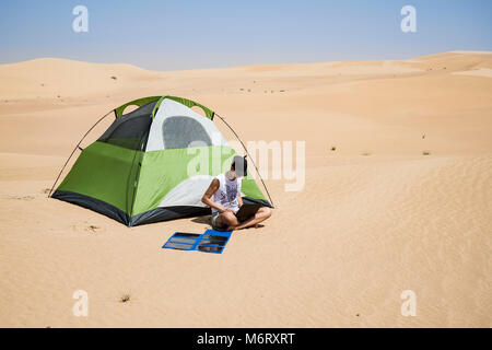 Eine Frau arbeitet ferngesteuert auf einem Campingplatz in der Wüste mit einem flexiblen Solarladegerät, Selbstvertrauen und umweltfreundlichem Wohnen mit Kopierraum Stockfoto