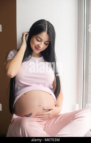Portrait von lächelnden schwangere Frau sitzen in der Fensterbank Stockfoto