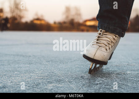 Ein junges Mädchen in der Skates auf einem zugefrorenen Teich auf Eis. Schönen Wintertag, schöner Hintergrund verschwommen. Stockfoto