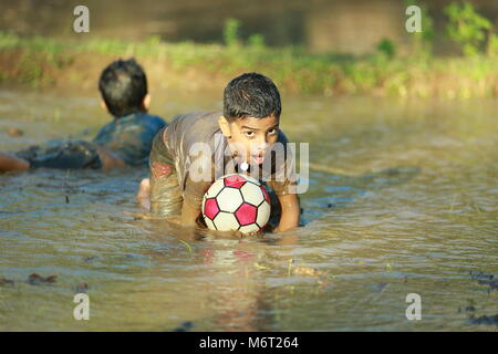 Glückliche Kindheit, Schlamm Spielen, Fußball, Spaß mit Natur, Kindheit genießen, Kinder Fußball, Erinnerungen, Spaß, Kinder Zyklus, Baum mit Junge, Spiel Stockfoto