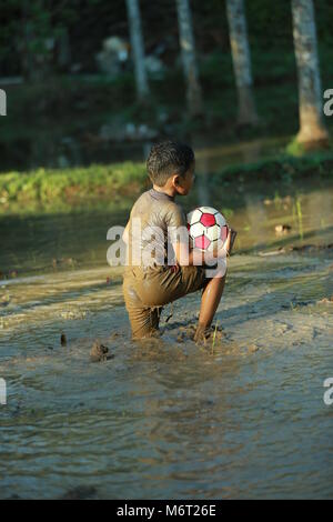 Glückliche Kindheit, Schlamm Spielen, Fußball, Spaß mit Natur, Kindheit genießen, Kinder Fußball, Erinnerungen, Spaß, Kinder Zyklus, Baum mit Junge, Spiel Stockfoto