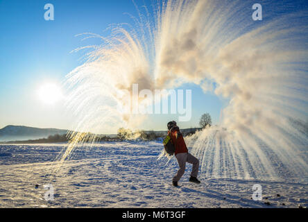 Ein Mann warf heißes Wasser auf Eis Fluss in Mohe, China. Stockfoto