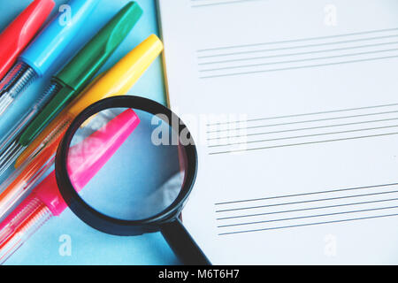 Farbige Stifte und Lupe auf einem weißen Blatt von Notepad für Text Stockfoto