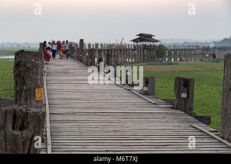 Einige Leute im U-Bein Brücke in Amarapura in der Nähe von Mandalay in Myanmar. Es ist die älteste und längste Teakholz Brücke der Welt. Fokus auf den Vordergrund Stockfoto
