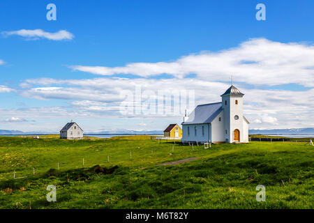 Flateyjarkirkja Kirche und paar Wohn häuser mit Wiese vorne im Meer und Fjord mit blauen Himmel im Hintergrund, Flatey, Island Stockfoto