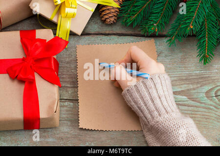 Woman's Hand schreiben einen Brief auf einem Holz- Hintergrund mit Weihnachtsschmuck. Stockfoto