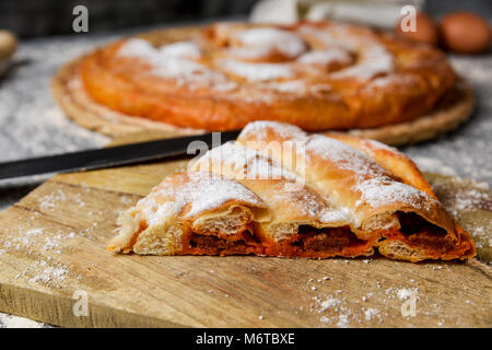 Nahaufnahme von einem Stück ensaimada, ein Gebäck, das typisch für Mallorca, Spanien, gefüllt mit sobrassada, auf einem rustikalen Holztisch Stockfoto