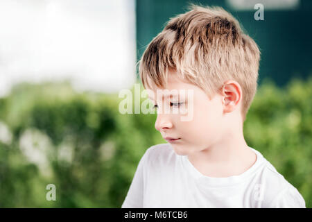 Kleinen Niedlichen kaukasischen blonde Junge, ein bisschen traurig oder schüchtern, in einem Garten irgendwo beiseite. Stockfoto