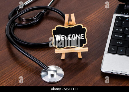 Schreibtisch des Arztes mit Stethoskop und roten Herzen und Tafel mit einem Text: Willkommen. Stockfoto