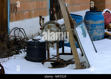 Die alte blaue aus durchsichtigem Kunststoff ist in den Schnee auf einer verlassenen und zerstörten Fabrik im Chaos geworfen. Zerstörung und Vandalismus. In der Ukraine. Stockfoto