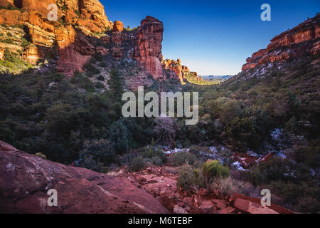 Atemberaubende Aussicht auf Fay Canyon von oben die Baumkronen mit Patches von Schnee auf dem Boden und majestätischen Blick auf Bell Rock und den Courthouse Butte in der Dis Stockfoto