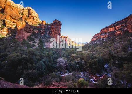 Atemberaubende Aussicht auf Fay Canyon von oben die Baumkronen mit Patches von Schnee auf dem Boden und majestätischen Blick auf Bell Rock und den Courthouse Butte in der Dis Stockfoto